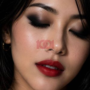 A close-up of a woman with dark eye makeup and bold red lips, showcasing flawless skin and a serene expression.