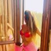 A woman in a red bikini stands by a window, sunlight illuminating her silhouette and flowing hair.