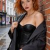 Ritratto di una giovane donna con capelli rossi, abbigliamento elegante e uno sguardo magnetico, in un ambiente urbano.