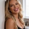 Ritratto di donna sorridente con capelli ondulati e top nero, in un ambiente luminoso.