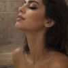 A woman with wet hair and glistening skin enjoys a serene moment, illuminated by soft lighting and steam.