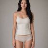Modella in top e pantaloni intimi chiari, con sfondo neutro. Capelli lunghi e ondulati.