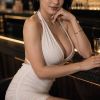 A woman in a stylish white dress poses elegantly at a bar, exuding confidence and charm.