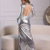 A woman poses in a silver, long-sleeve gown with an open back, showcasing a modern and elegant style.