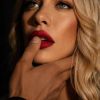 Donna con labbra rosse e occhi chiari, un mano maschile la tiene delicatamente per il viso. Sfondo scuro.