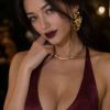 Donna con abito bordeaux, orecchini dorati e labbra scure, gesto di mano sul viso in un ambiente elegante.