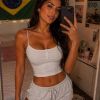 A woman takes a selfie in casual clothing, with a Brazilian flag and decor in the background.
