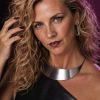 A woman with curly hair and bold makeup poses elegantly, wearing stylish jewelry and a sleek black outfit.