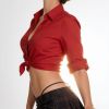 Una donna con camicia rossa e gonna a quadri, posando con eleganza su sfondo chiaro.