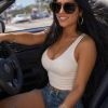 A woman in sunglasses smiles while sitting in a convertible car, enjoying a sunny day outdoors.