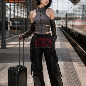 A stylish individual stands at a train station with a black suitcase, wearing a trendy outfit.