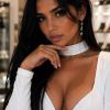 A woman in a white dress poses confidently, showcasing her long hair and elegant earrings.