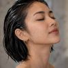 A close-up of a woman with short, wet hair, eyes closed, and water dripping down her face and neck.