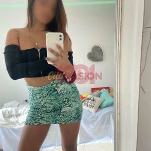 Una giovane donna si fotografa allo specchio indossando un top nero e una mini gonna verde a motivo serpente.