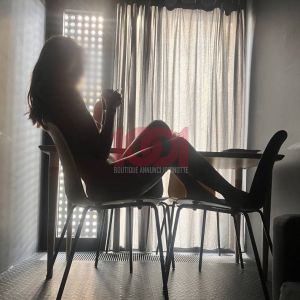 A silhouette of a person sitting on a chair, holding a cup, with bright light and curtains in the background.