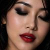 A close-up of a woman with dark eye makeup and bold red lips, showcasing flawless skin and a serene expression.