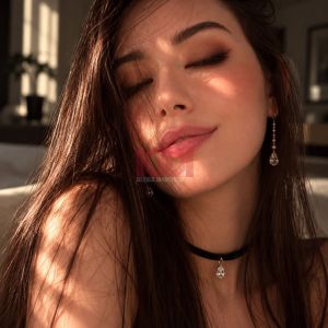 Ritratto di una giovane donna con lunghi capelli castani, orecchini brillanti e trucco sofisticato in luce naturale.