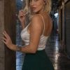 Donna con capelli biondi e corti, vestita con top bianco e gonna verde, in una strada bagnata sotto la pioggia.
