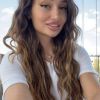 Ritratto di una giovane donna con lunghi capelli ricci, sorridente, in un ambiente luminoso e naturale.