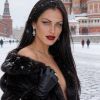 Una donna con capelli scuri e lunghi indossa un cappotto di pelliccia, in un paesaggio innevato con cattedrali.