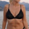 Una donna in bikini nero sorride, mentre il mare e le montagne fanno da sfondo a un tramonto sereno.