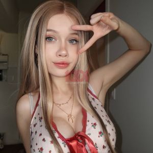 Ragazza sorridente con capelli lunghi e biondi, indossa un top floreale e fa un segno di pace con la mano.