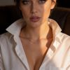 Ritratto di donna con camicia bianca, sguardo intenso e trucco elegante in luce naturale.