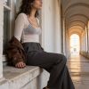 Una donna elegante sieda su un muretto, indossando pantaloni grigi e tacchi rossi, in un'ambientazione architettonica.