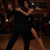 A couple elegantly dances tango on a wooden floor, showcasing emotion in a dimly lit, intimate setting.