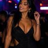 A woman in a sparkling black dress smiles and dances, illuminated by colorful club lights.