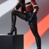 A confident model poses in a stylish red and cream jacket, black shorts, and knee-high boots against dramatic lighting.