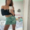 Una giovane donna si fotografa allo specchio indossando un top nero e una mini gonna verde a motivo serpente.