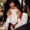 A woman playfully hides her smile behind a napkin while dining in an elegant restaurant.