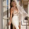 Una figura femminile elegante, con un abito satinato e una gonna aderente, si affaccia su un luminoso terrazzo.