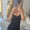 Una giovane donna si riflette nello specchio indossando un vestito nero, mentre tiene in mano un telefono.