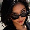A young woman in sunglasses poses confidently with a city background, showcasing her stylish, casual look.