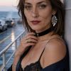 Donna con capelli castani ondulati in un top nero e orecchini, accanto a una balaustra su una nave.