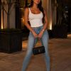 A stylish woman poses confidently at night, wearing a white top, jeans, and a black cap, holding a designer bag.