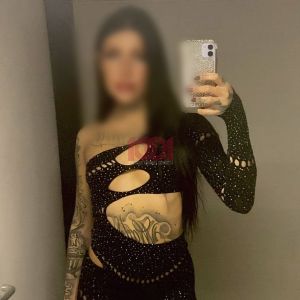 Una persona si riflette nello specchio indossando un outfit nero decorato con strass e con tatuaggi visibili.