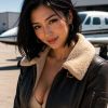 A woman smiles in a stylish jacket, standing near a small airplane under a clear blue sky.