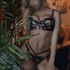 A model poses confidently in stylish lingerie, surrounded by tropical plants and soft lighting.