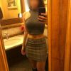 A person takes a mirror selfie in a stylish outfit, featuring a sleeveless top and a plaid mini skirt.